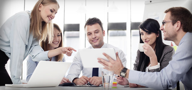 Group of co-workers smiling and laughing together while looking at a tablet