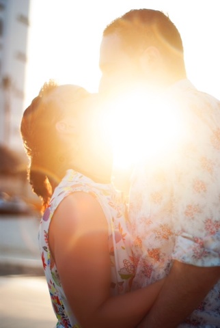 Man and woman kissing, the setting sun blocking the view of the kiss.