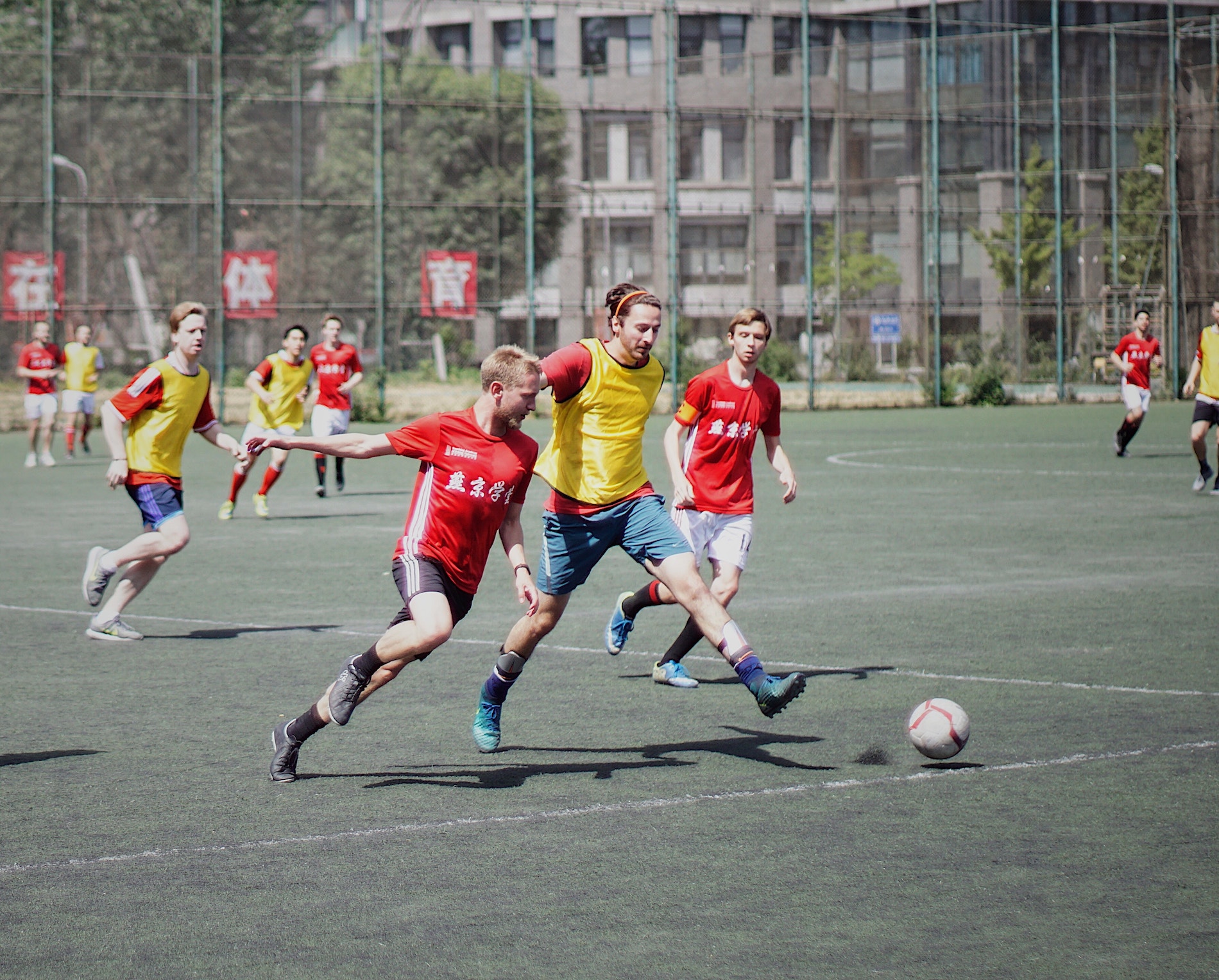 Three men- two of which are in red, the other in yellow - wearing soccer clothing with Chinese or Japanese kanji on it.