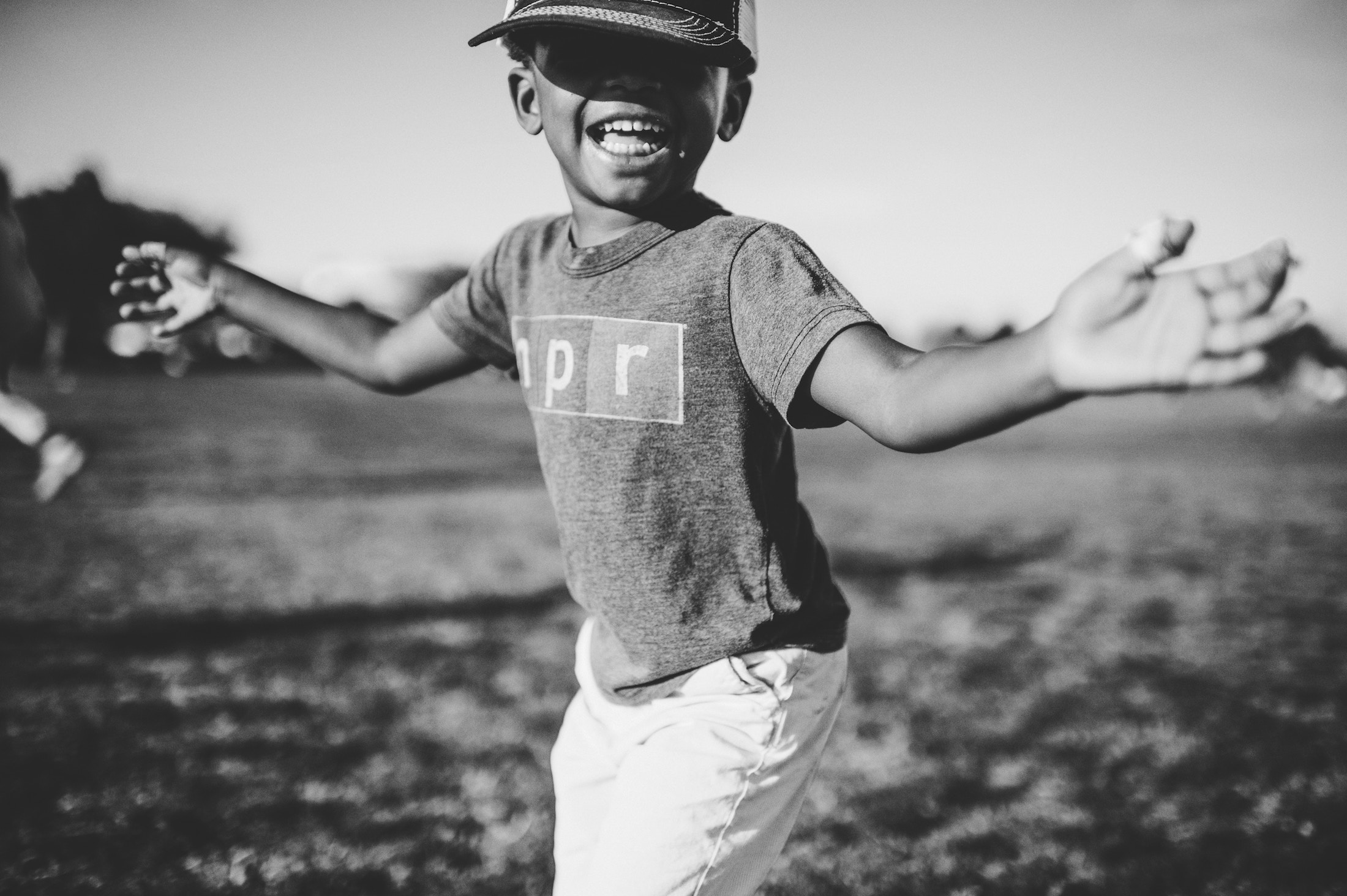 African American child with a baseball helmet on and his arms extended with a smile on his face.