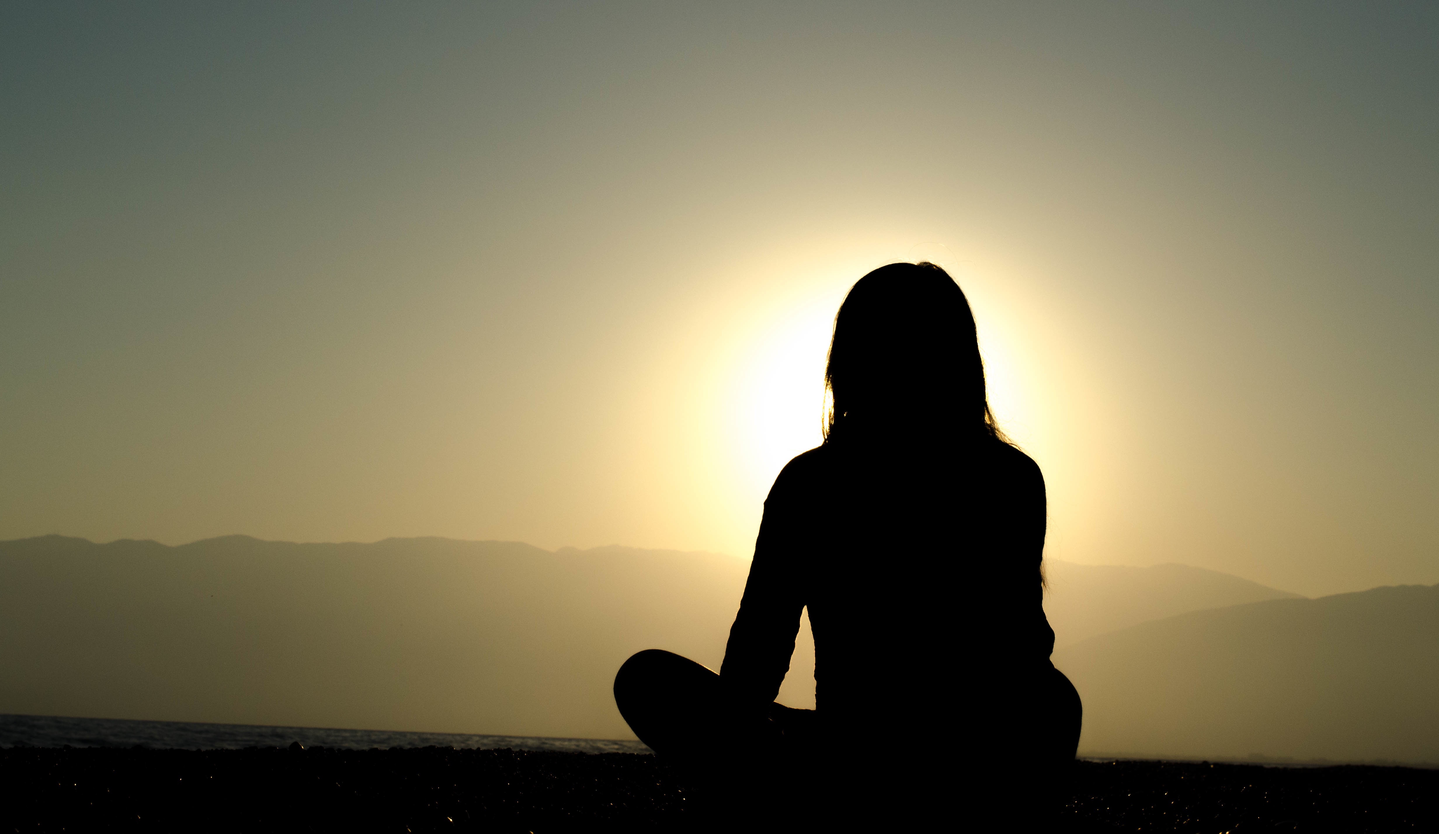 Silhouette of a woman meditating in front of a sunset.