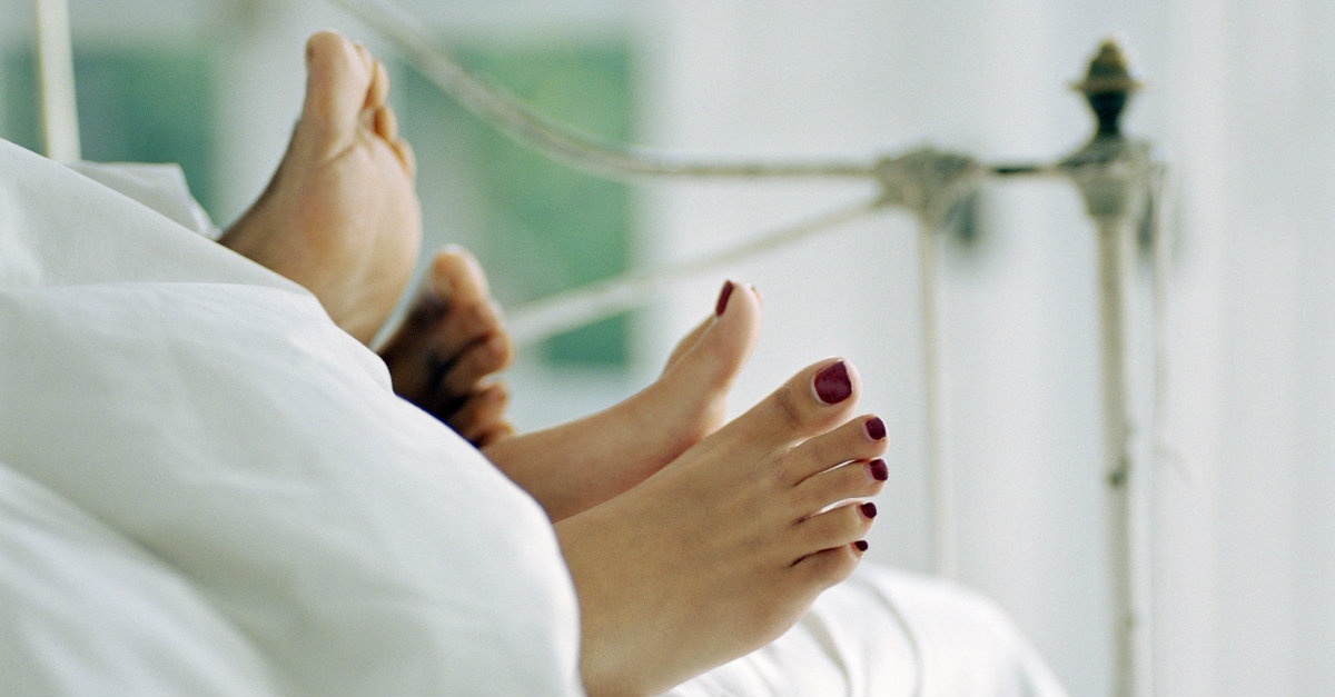 Two pairs of feet sticking out from under the comforter in bed