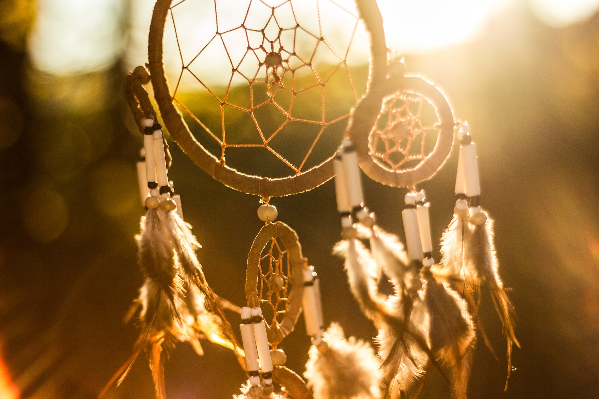 Dreamcatcher hanging outside in front of a bright sunset.