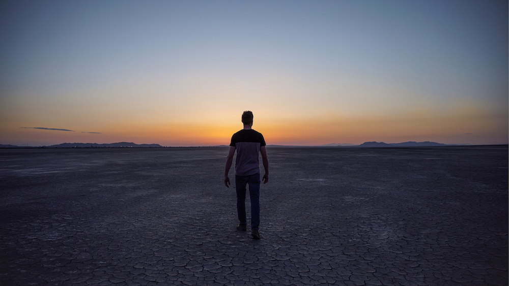 Picture from behind a man with his arms at his side, gazing at the sunset