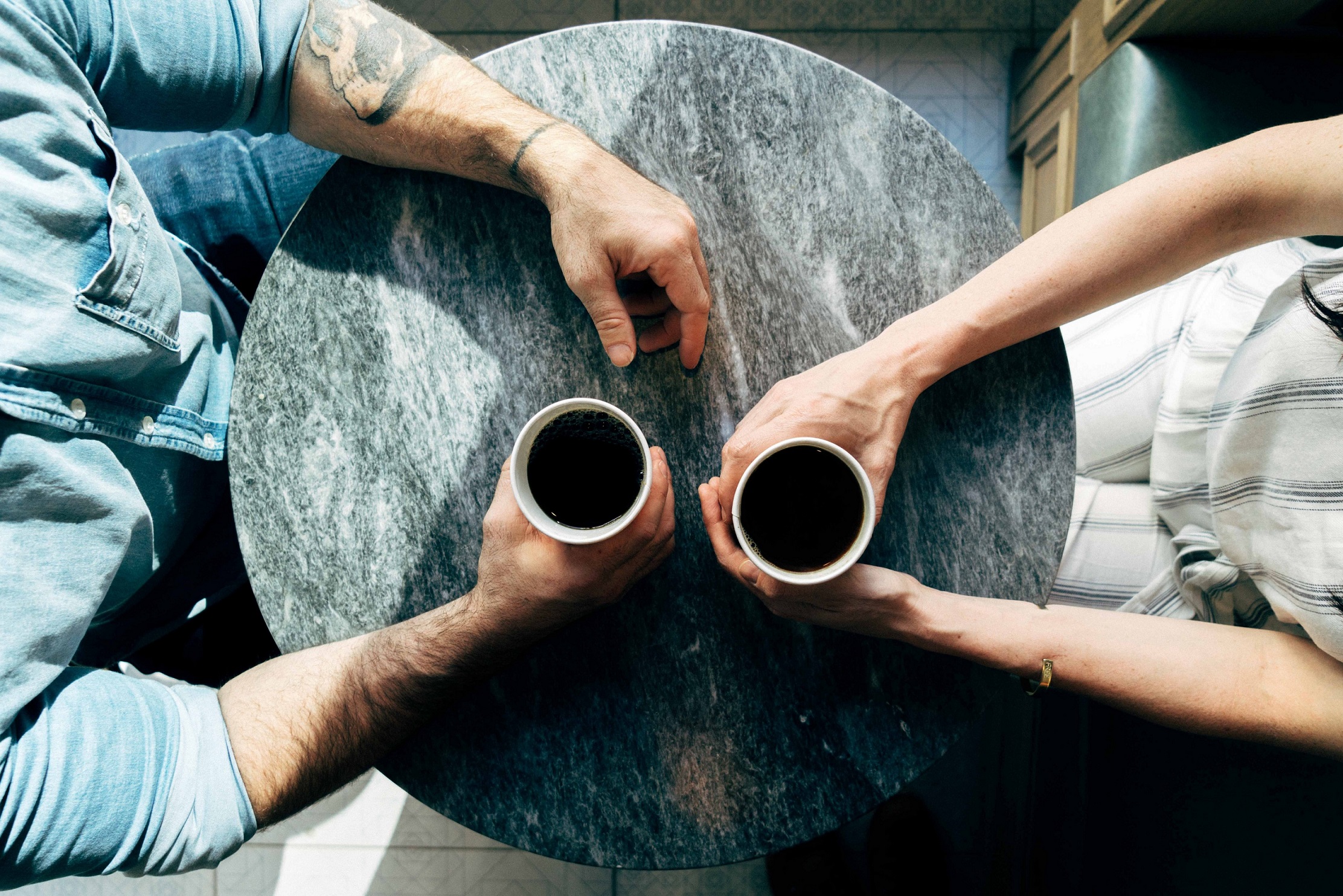 Above shot of woman and man holding coffee cups at a small marble table in a cafe