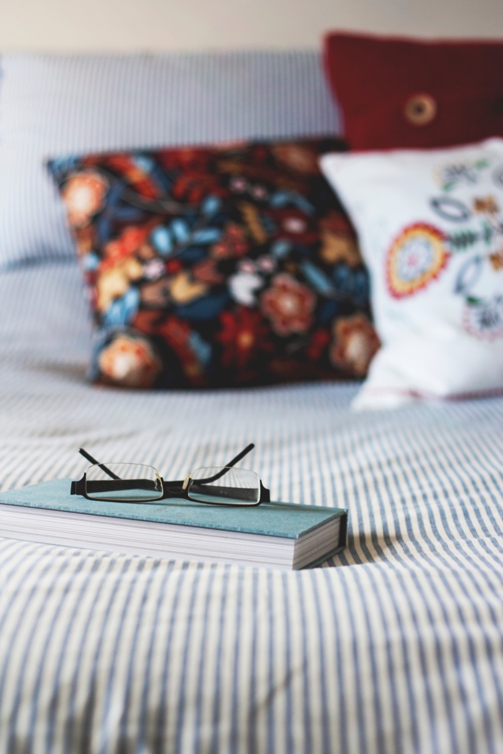Black glasses on top of a light-turquoise journal sitting on a bed with faded blue stipes.
