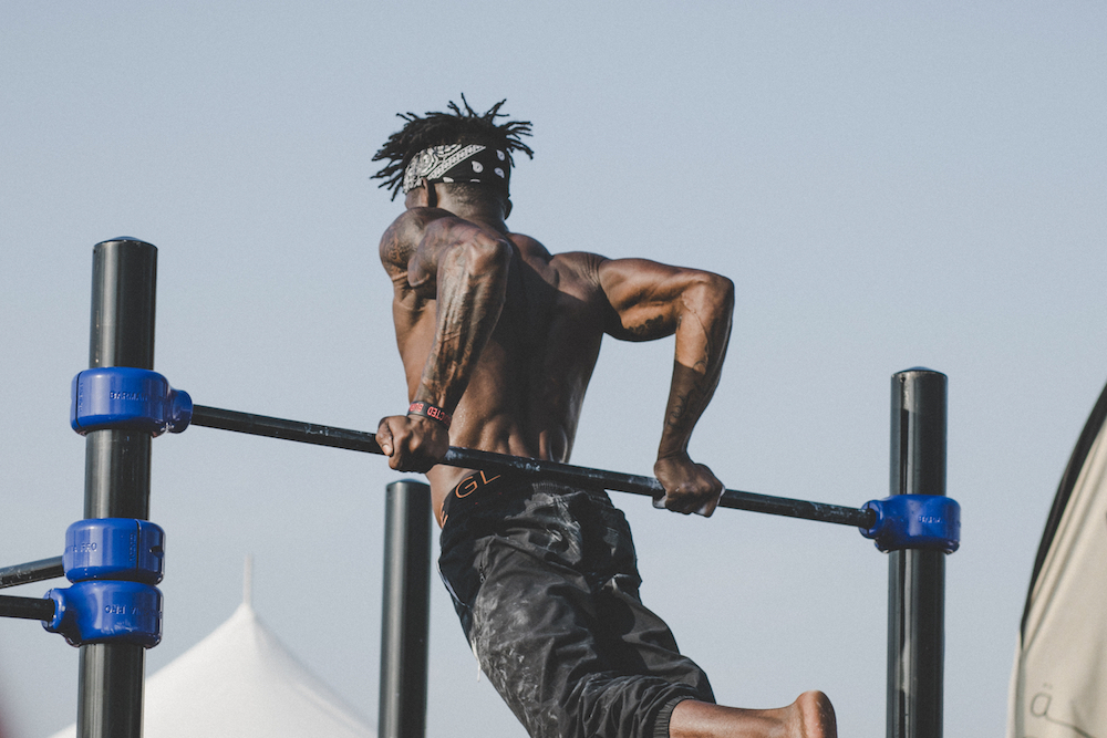 Shirtless African American man doing reverse pull-ups.