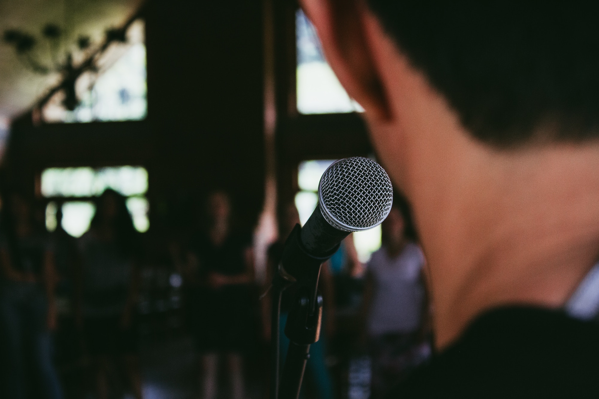 Back of man standing in front of a microphone with others looking toward him.