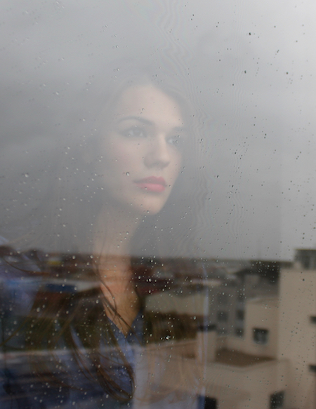 Woman standing behind a window with raindrops on it.