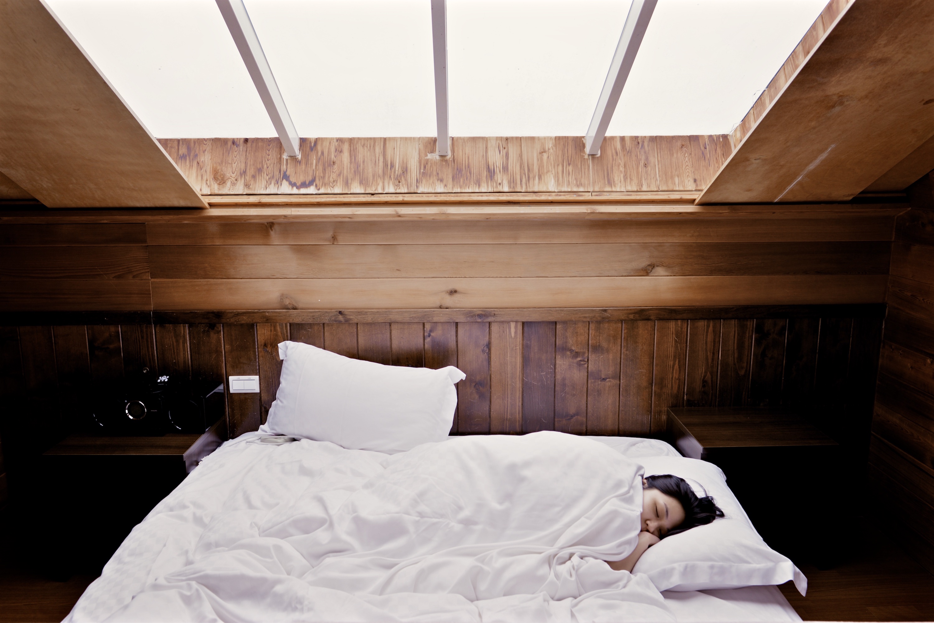 Asian woman sleeping under a sunroof with the white covers pulled up to her ear.