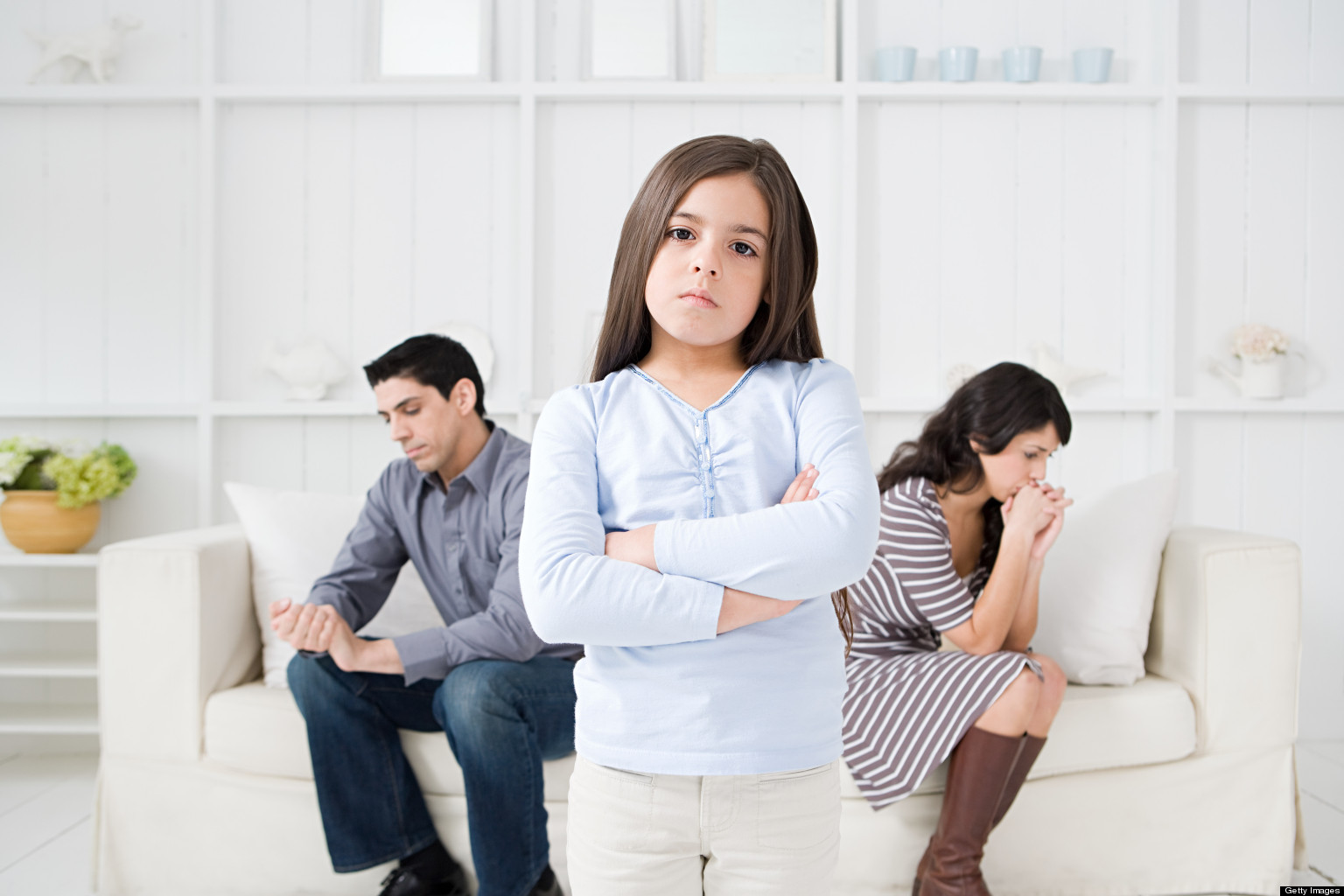 Sassy girl with her arms crossed in between her two struggling parents