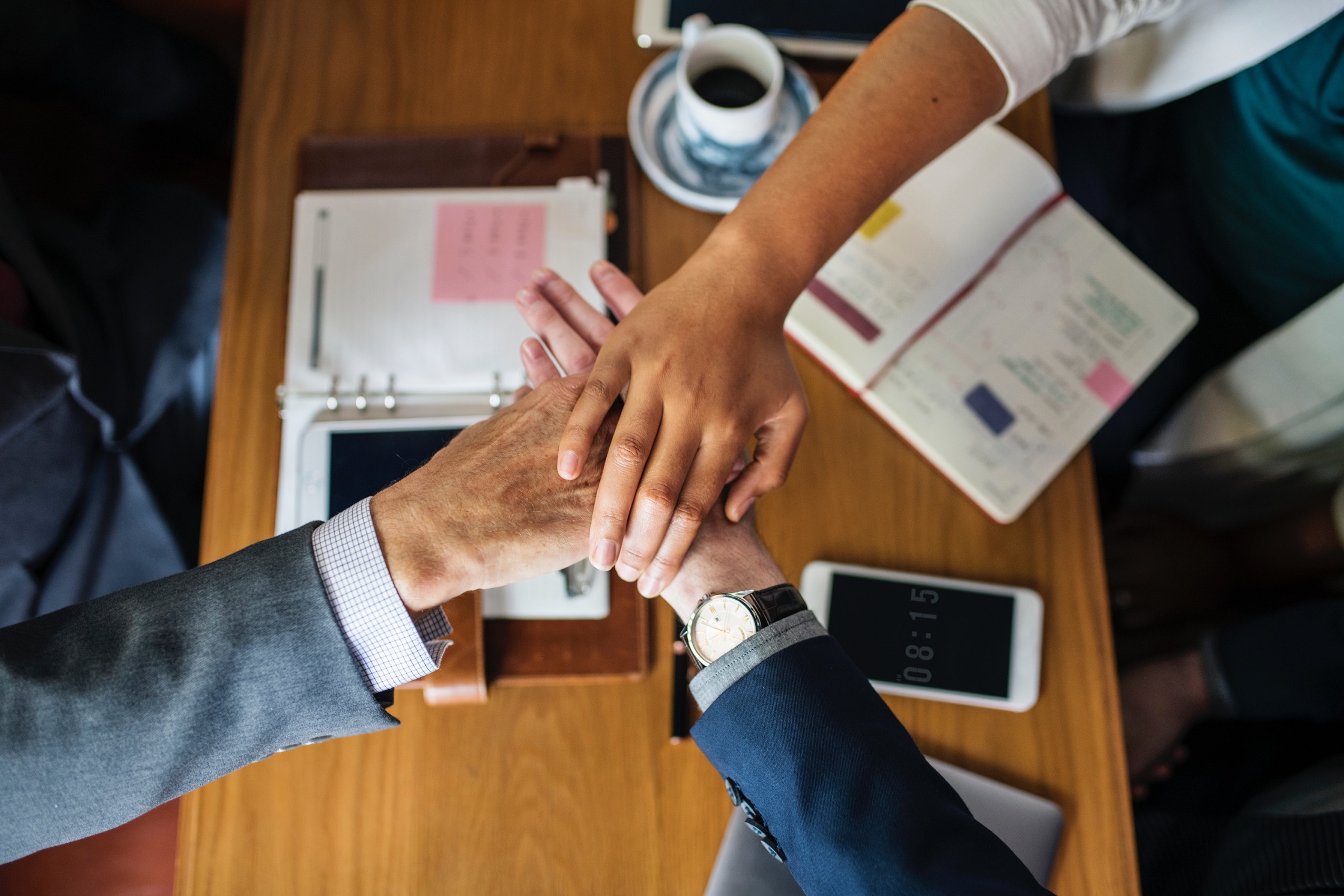 The hands of three coworkers on top of each other above a work table covered with Filofax planners and other work-related items.