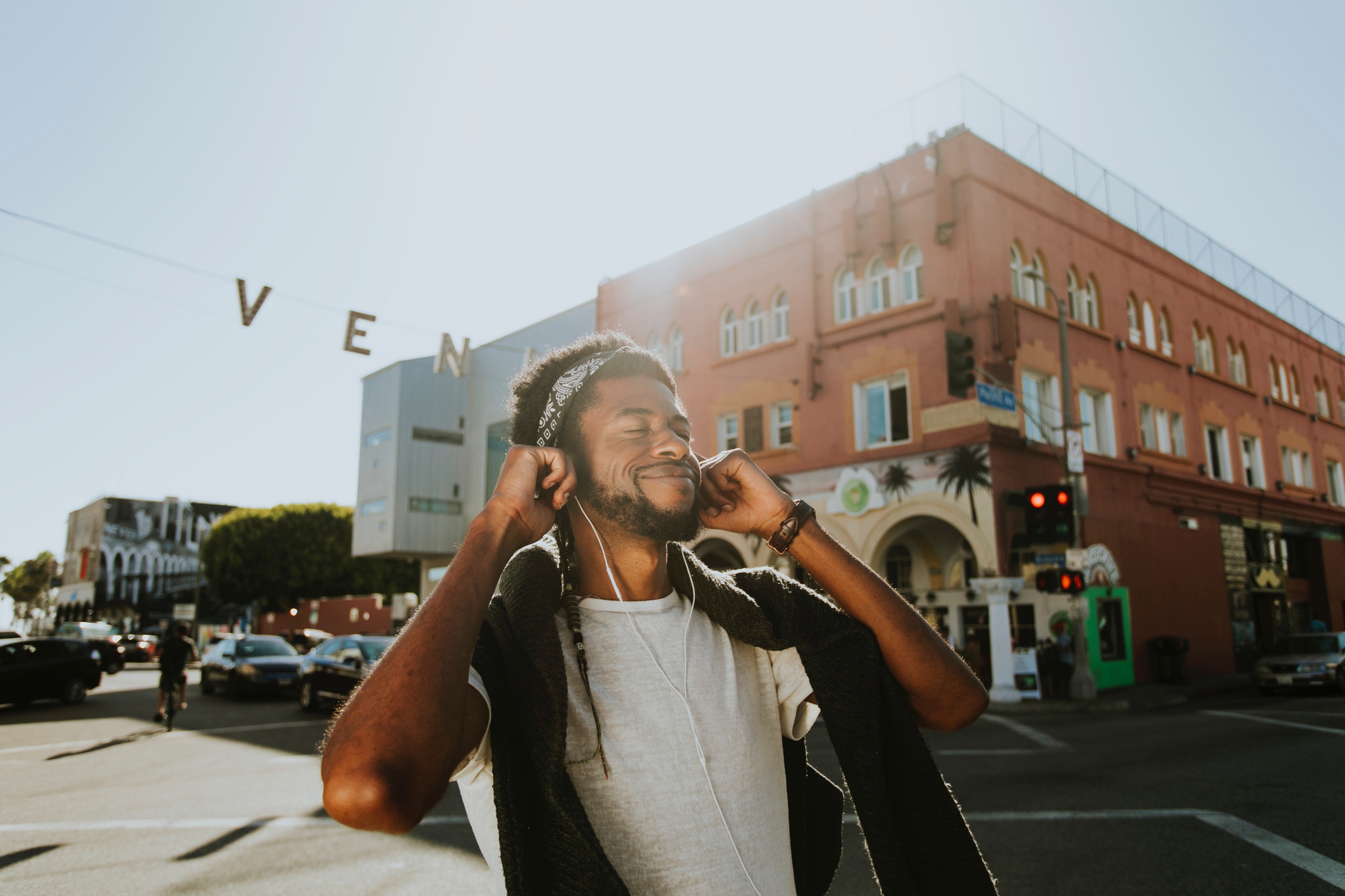 African American man smiling with eyes closed while holding on to in-ear headphones.