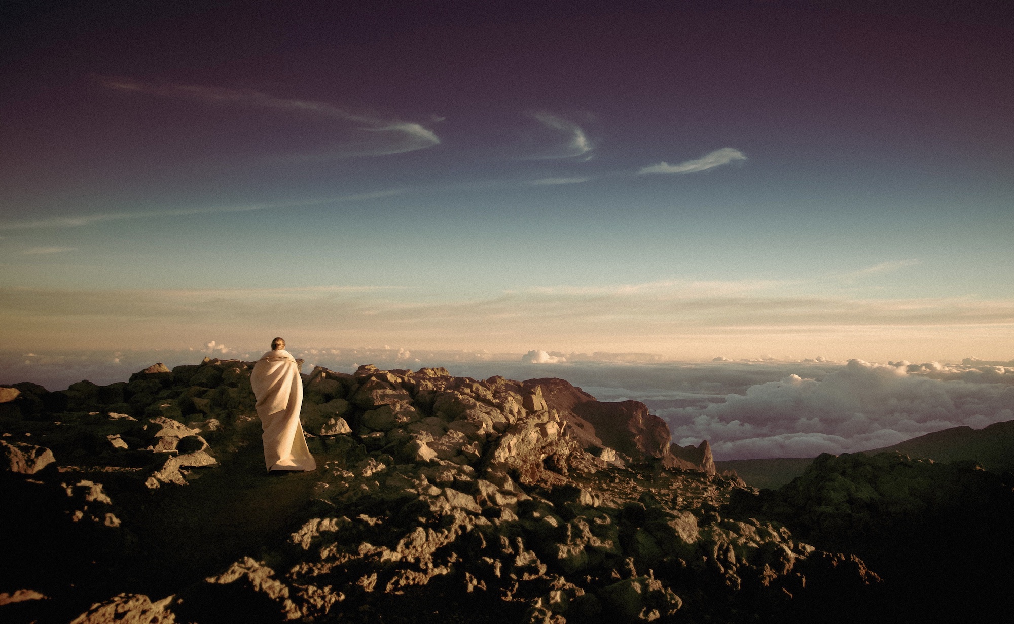 Monk in white wrap on top of a mountain, overlooking the clouds.