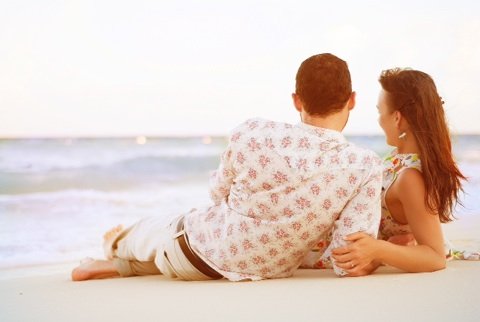 Shot from behind a couple laying on the beach watching the sunset