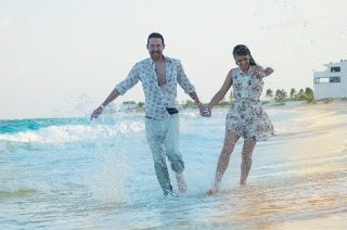 Man and woman holding hands splashing water with their feet while walking down the beach