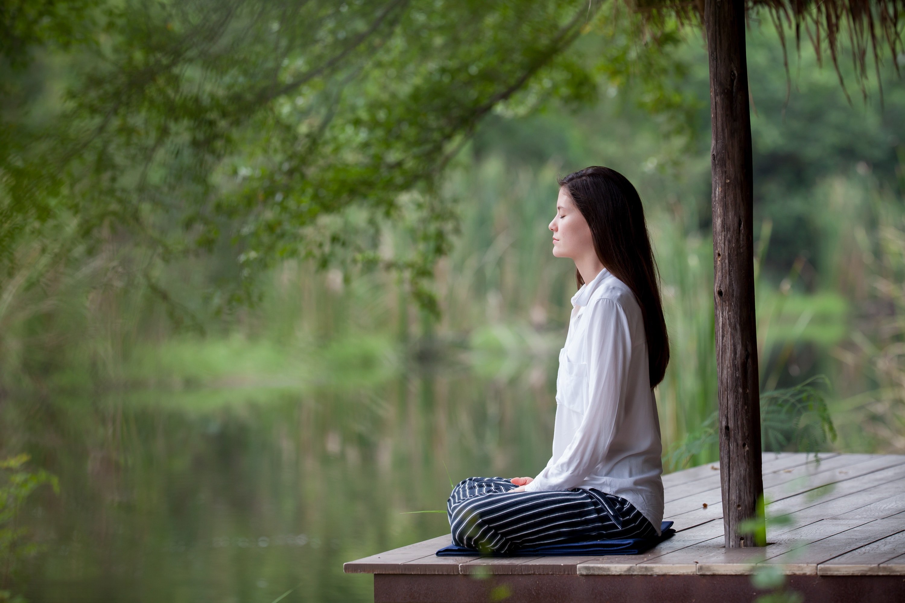 Long-haired woman meditating on the dock of a lake.
