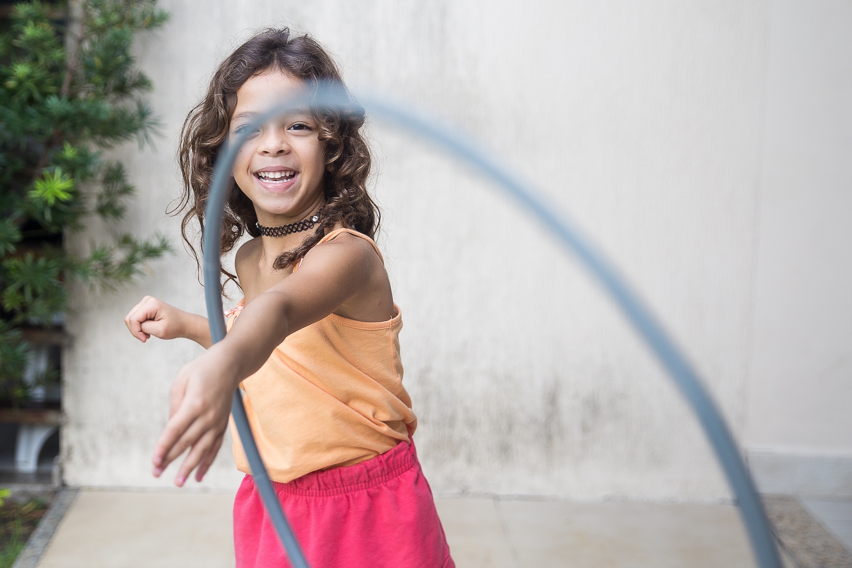 Girl in peach tank top and pink shorts tossing a hula hoop toward the camera.