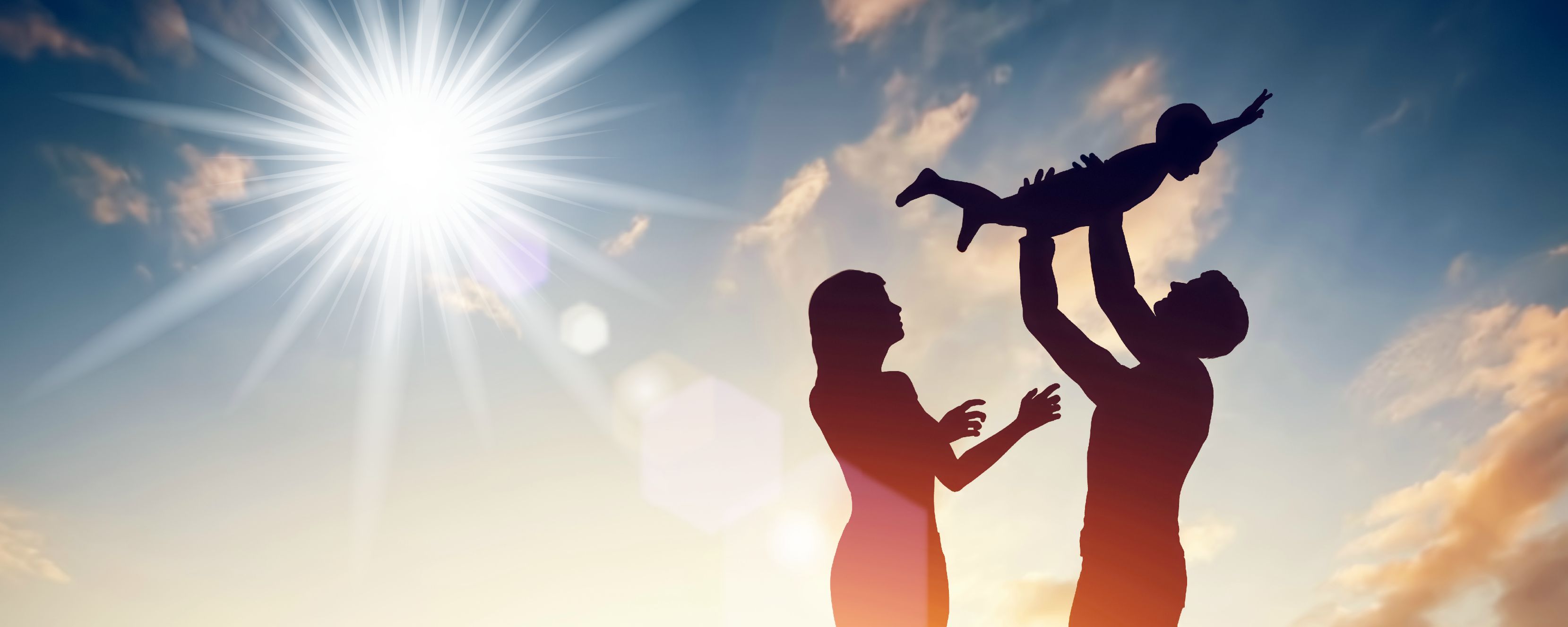 Silhouette of a father holding his son up in the air and the mother reaching for him