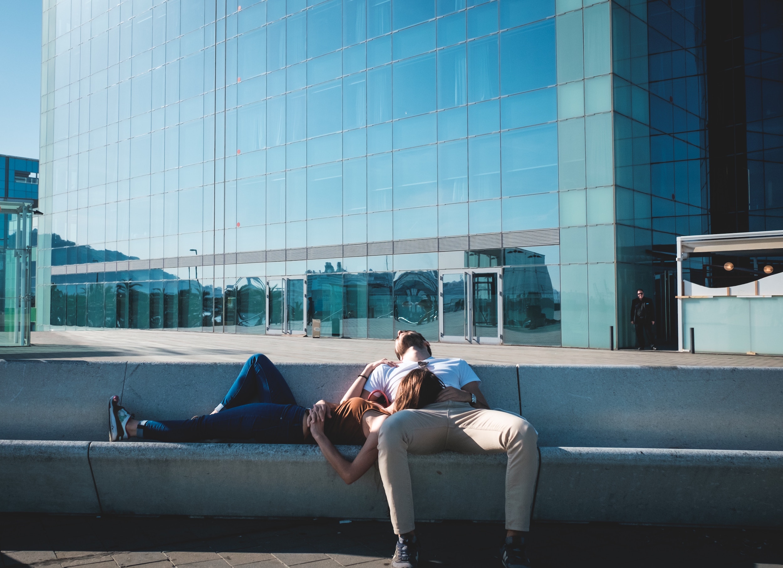 Man lying back on a concrete bench, his spouse laying horizontally with her head on his leg.