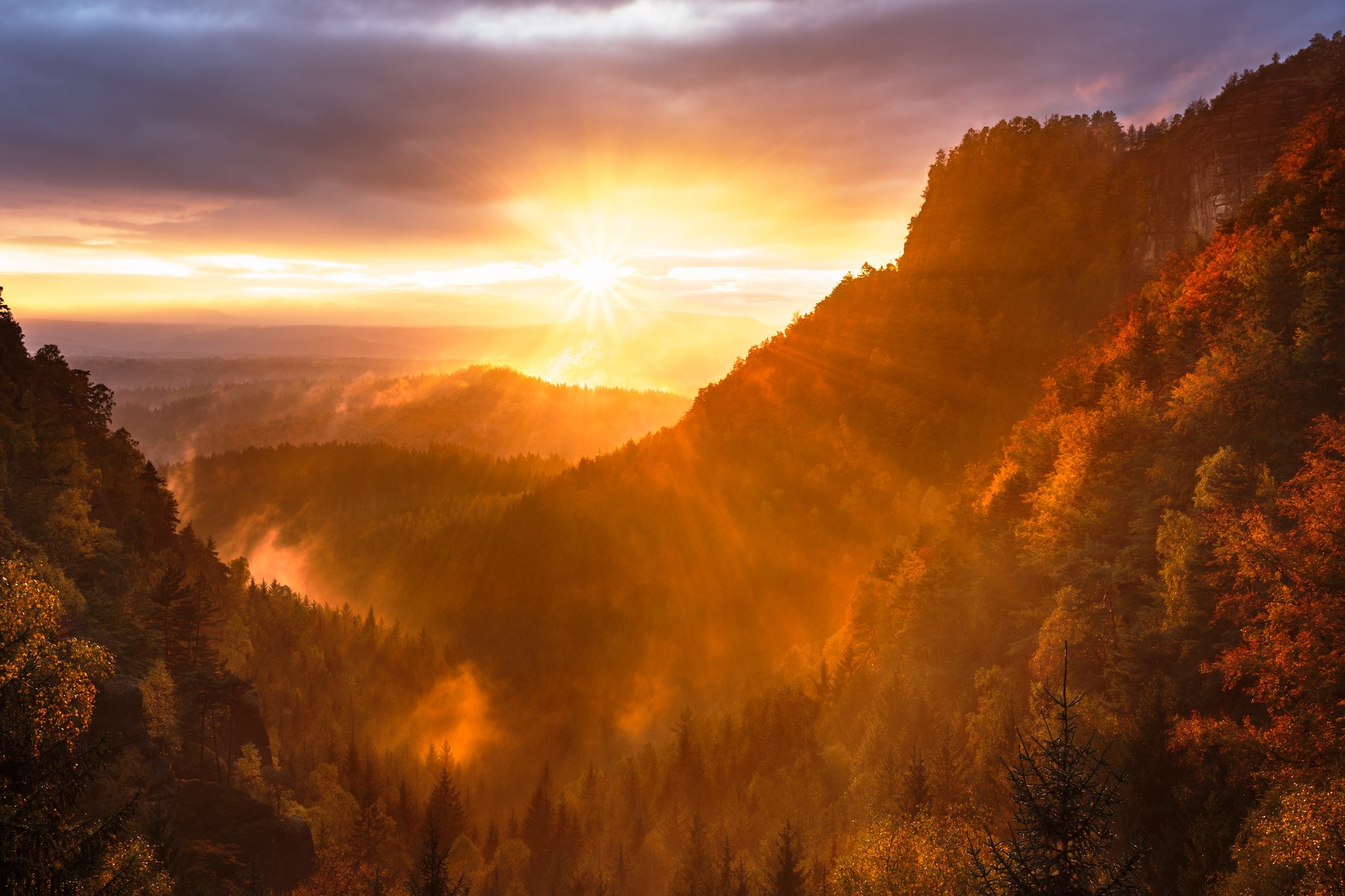 Orange sun with rays spread over a valley created by mountains