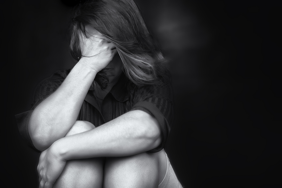 Black and white picture of a woman sitting with her right hand over her face and her let hand wrapped around her legs