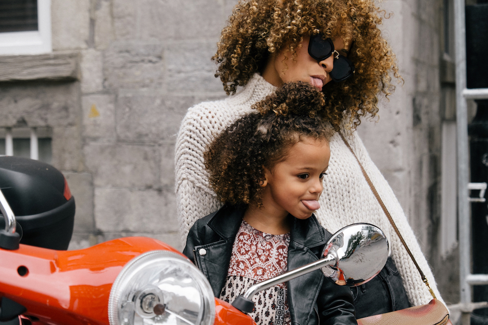 African American mother and daughter sticking their tongue out at the mirror on a motorcycle