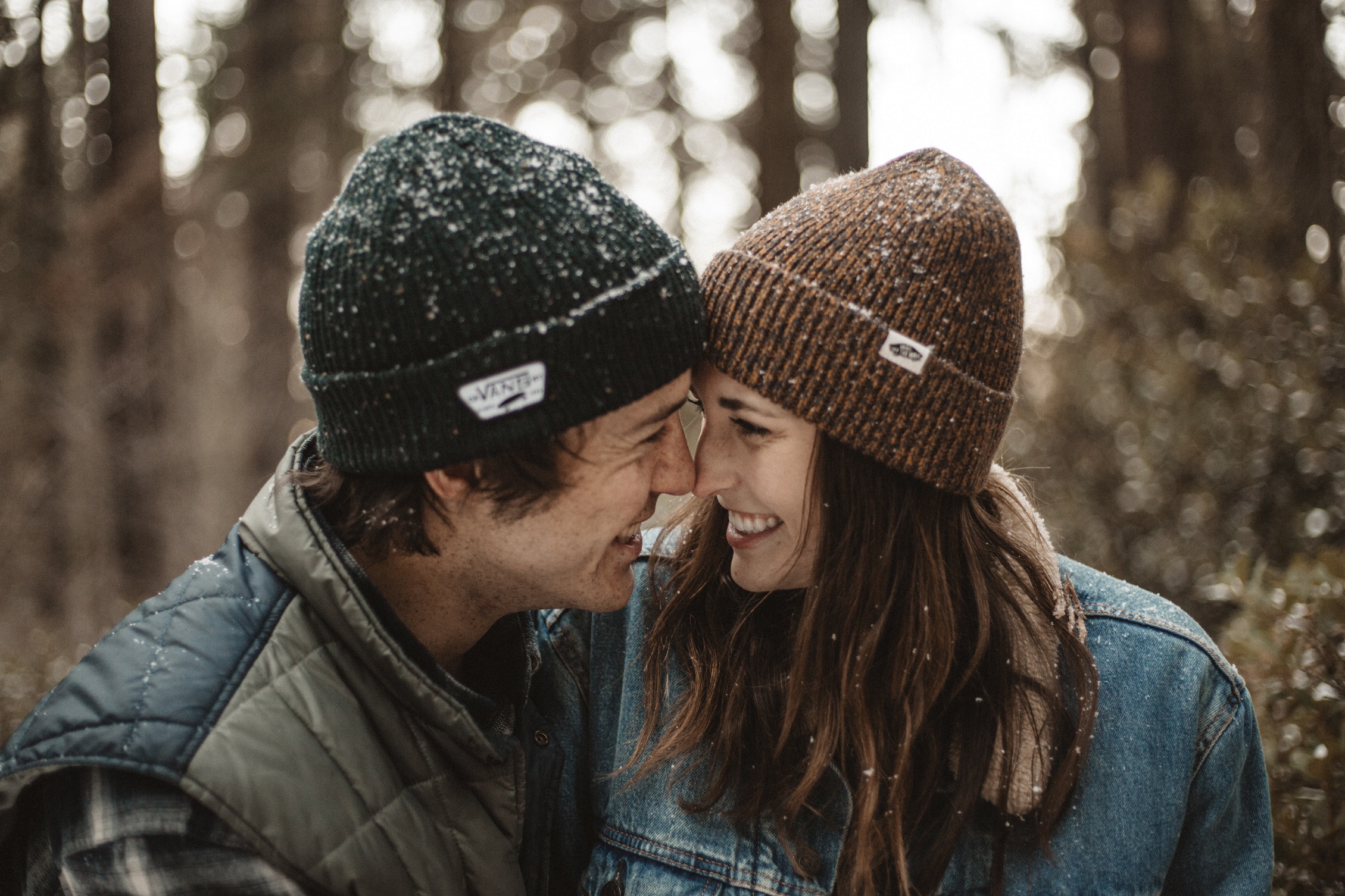Smiling couple looking at each other with touching noses amidst a light snowfall