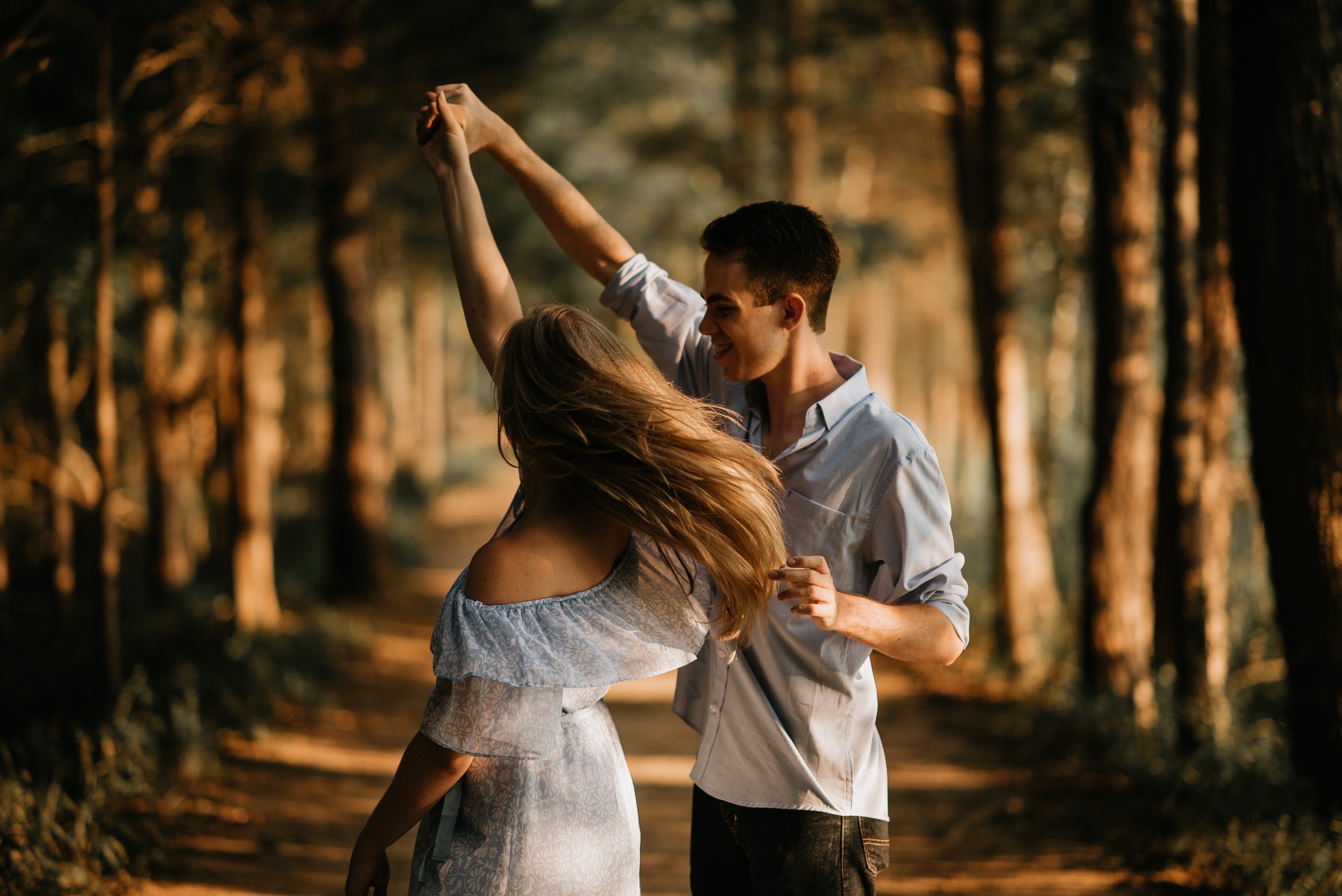 Couple dancing on a path in between a long column of trees.
