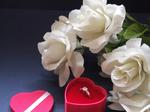 Four white roses surrounding a small red heart full of chocolates.