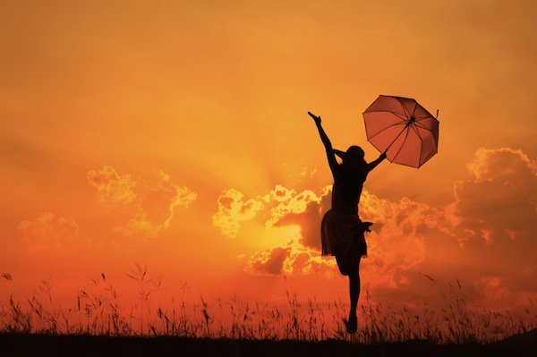 Silhouette of a woman in a dress holding an umbrella jumping